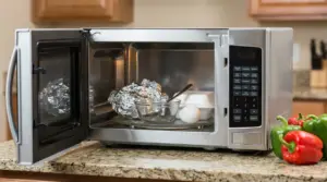 Microonde aperto con foglio di alluminio, ciotola di vetro, cucchiaio di metallo e uovo sul piatto girevole