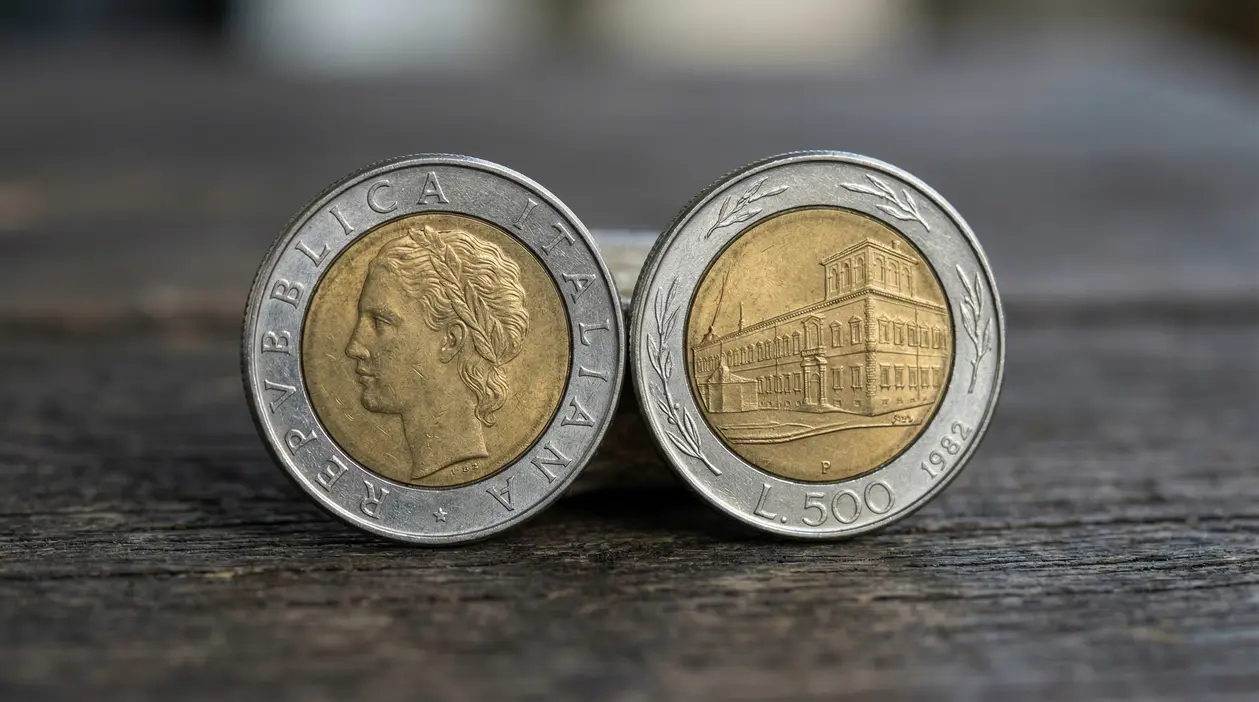 Due monete da 500 lire bimetalliche del 1982 affiancate, con profilo e edificio, su superficie in legno