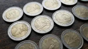 Monete da 2 euro, alcune commemorative, disposte su un tavolo in legno, tema collezionismo e pezzi rari