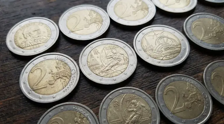 Monete da 2 euro, alcune commemorative, disposte su un tavolo in legno, tema collezionismo e pezzi rari