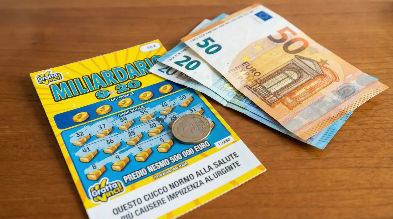 Gratta e vinci con moneta e banconote in euro su un tavolo, simbolo di vincite e tasse sui premi